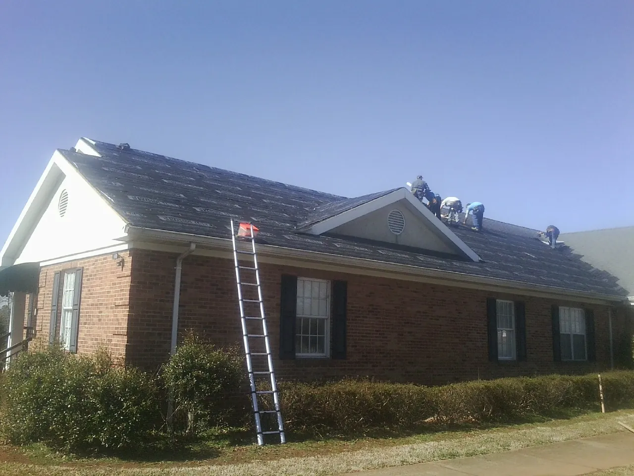 Crew tearing shingles off a brick ranch roof with a ladder set — Emergency Roof Repair work by our crew in Pleasantville