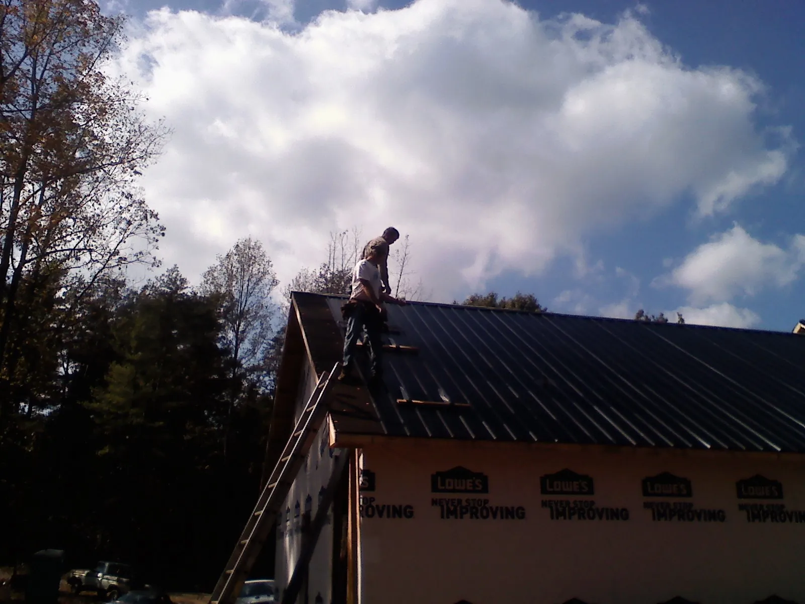 Roofer fastening dark metal panels high against a cloudy sky, from a Roof Inspection job in Pleasantville