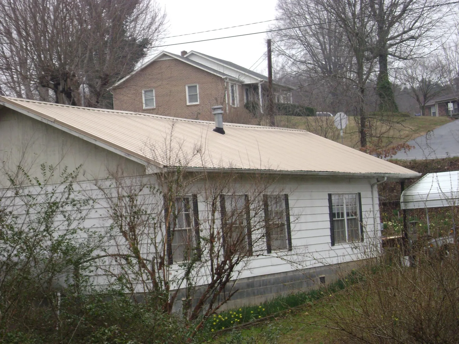 Tan metal roof on a white sided house set into a hillside — Commercial Roofing by Roofing Brothers in Pleasantville